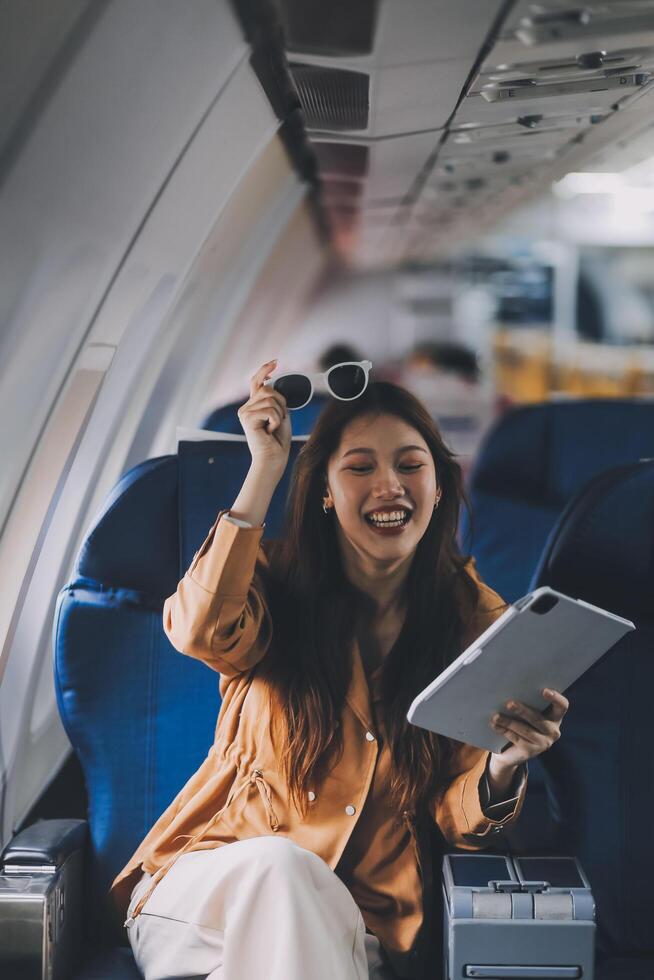 Joyful asian woman sits in the airplane and using tablet while go to travel photo