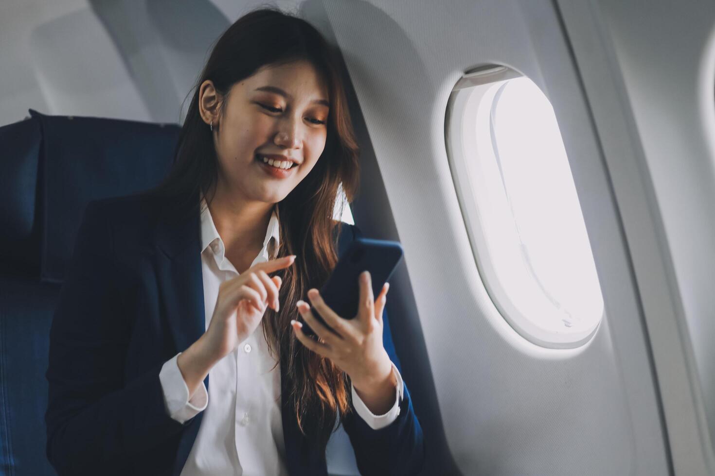 A young Asian female airplane passenger sits by the window during the flight, holding her boarding pass, with her carry-on luggage stored overhead, wearing her seatbelt, and enjoying the journey. photo