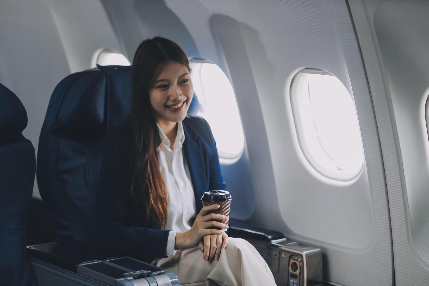 Young Asian female tourist traveling alone on a plane is drinking hot coffee and looking out the window. photo