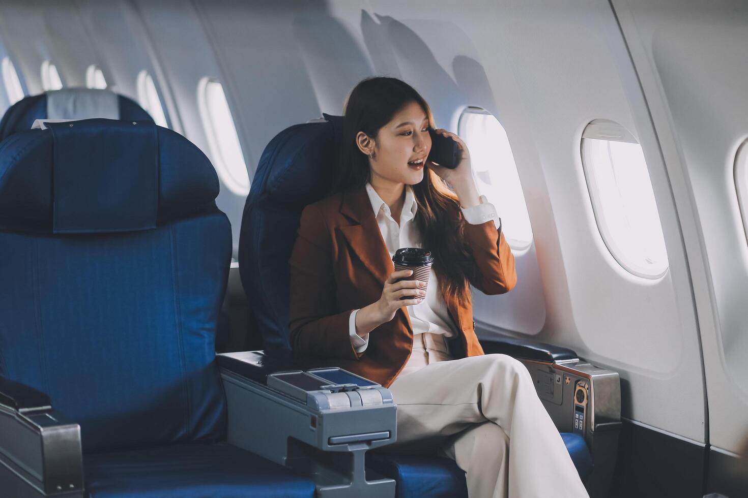 Asian woman looking at phone while sitting on airplane Technology female travelers using mobile smartphones, online apps, and the internet while sitting in airplane seats during travel. photo