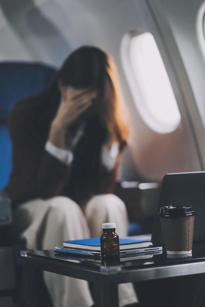 Photo of a frustrated woman sitting on an airplane with her head in her hands. Asian woman sitting in a seat in airplane