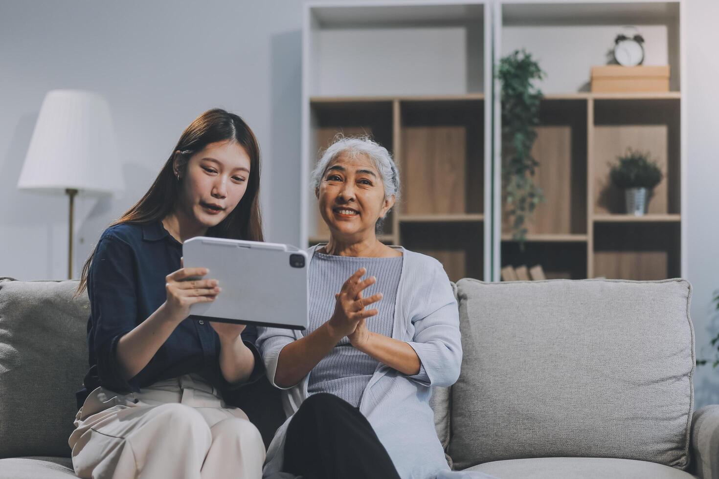 Happy grownup daughter showing content on tablet to mature mother. Two family generations women with digital computer gadget resting on couch together, watching videos, making call photo