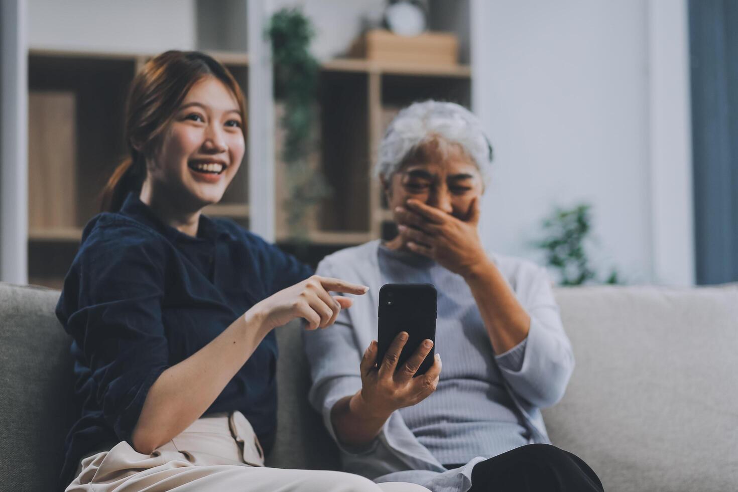 Cheerful mother and pretty teenager kid relaxing at cozy home, using mobile phone for Internet communication, resting on sofa with digital gadget, enjoying leisure, looking at camera photo
