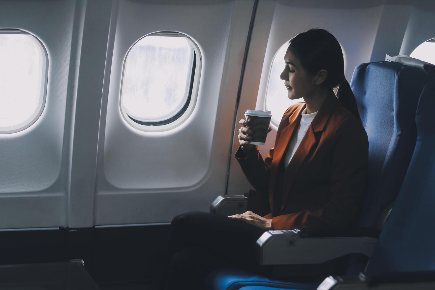 Young Asian female tourist traveling alone on a plane is drinking hot coffee and looking out the window. photo
