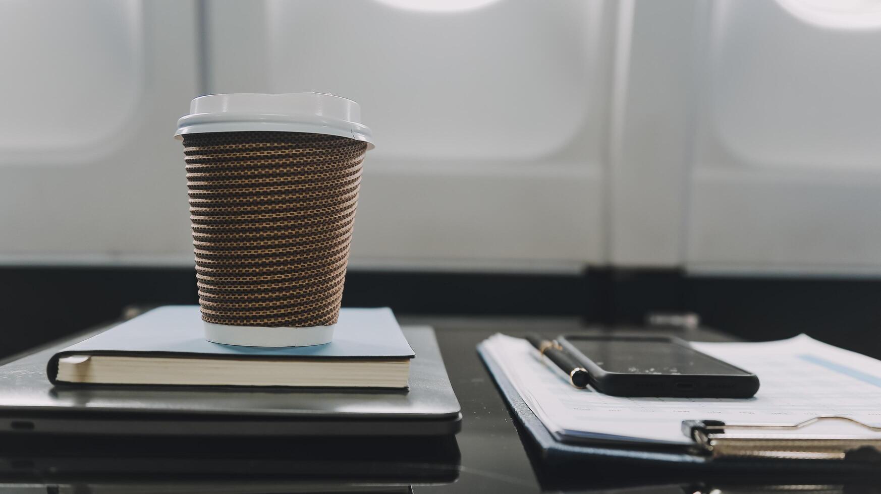 Cup of coffee with laptop and notebooks on table in airplane photo