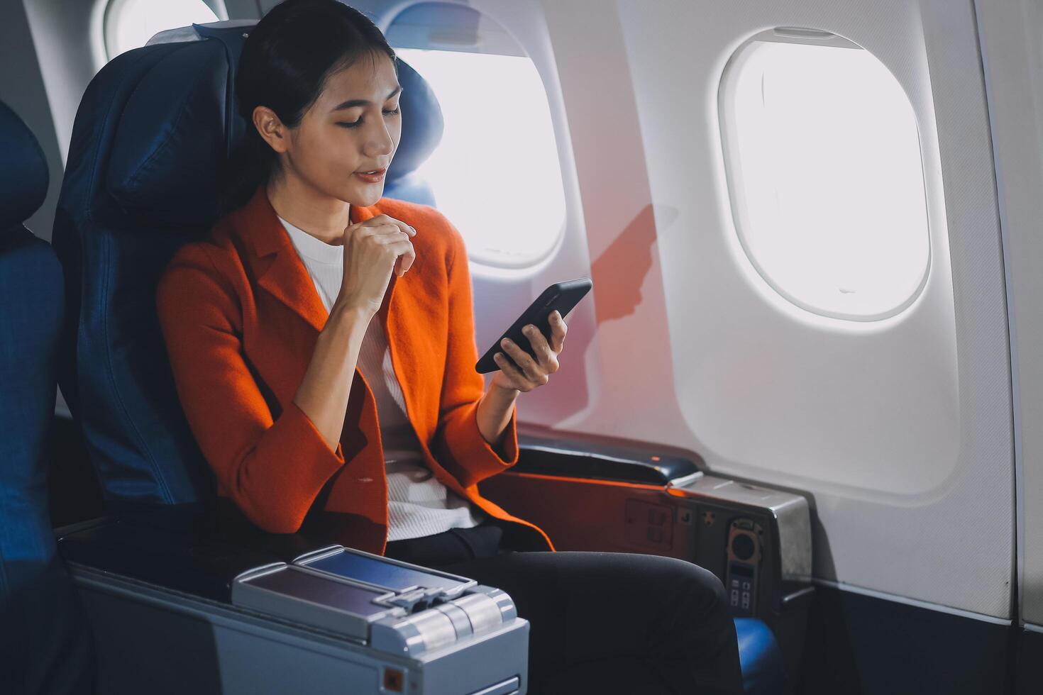 Young Asian woman uses mobile phone to check news information Sitting near the window in business class, airplane class during flight, travel and business concept photo