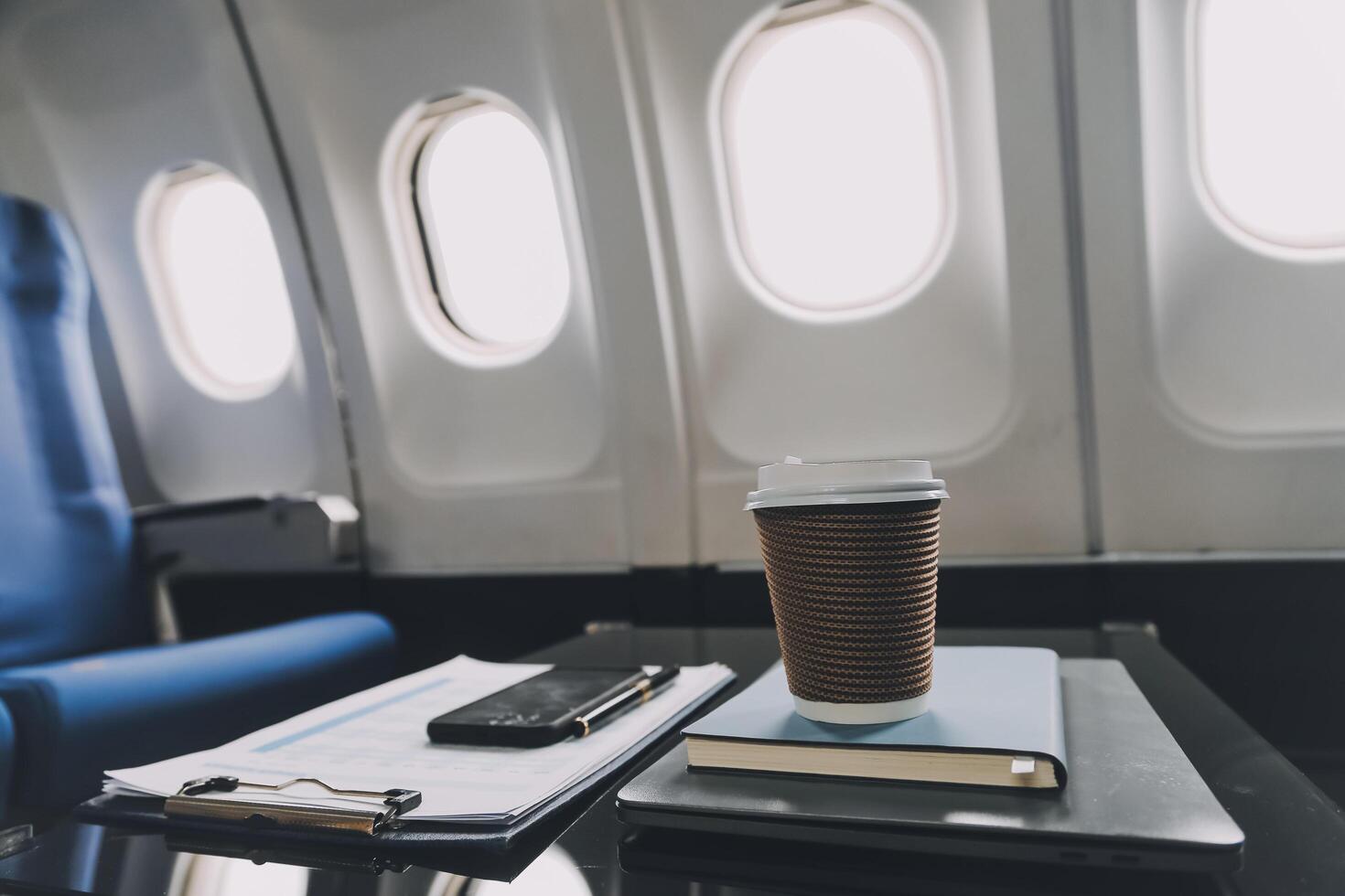 Cup of coffee with laptop and notebooks on table in airplane photo