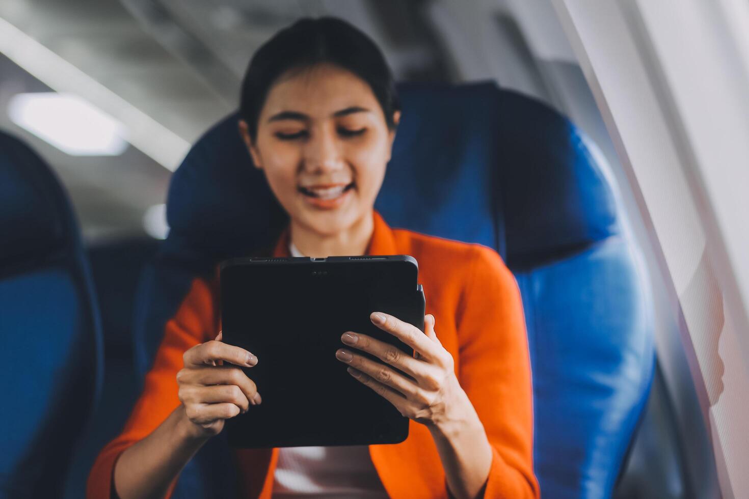 Young asian businesswoman in formal clothes working using tablet with smart pen while sitting in airplane cabin near window traveling to another place photo
