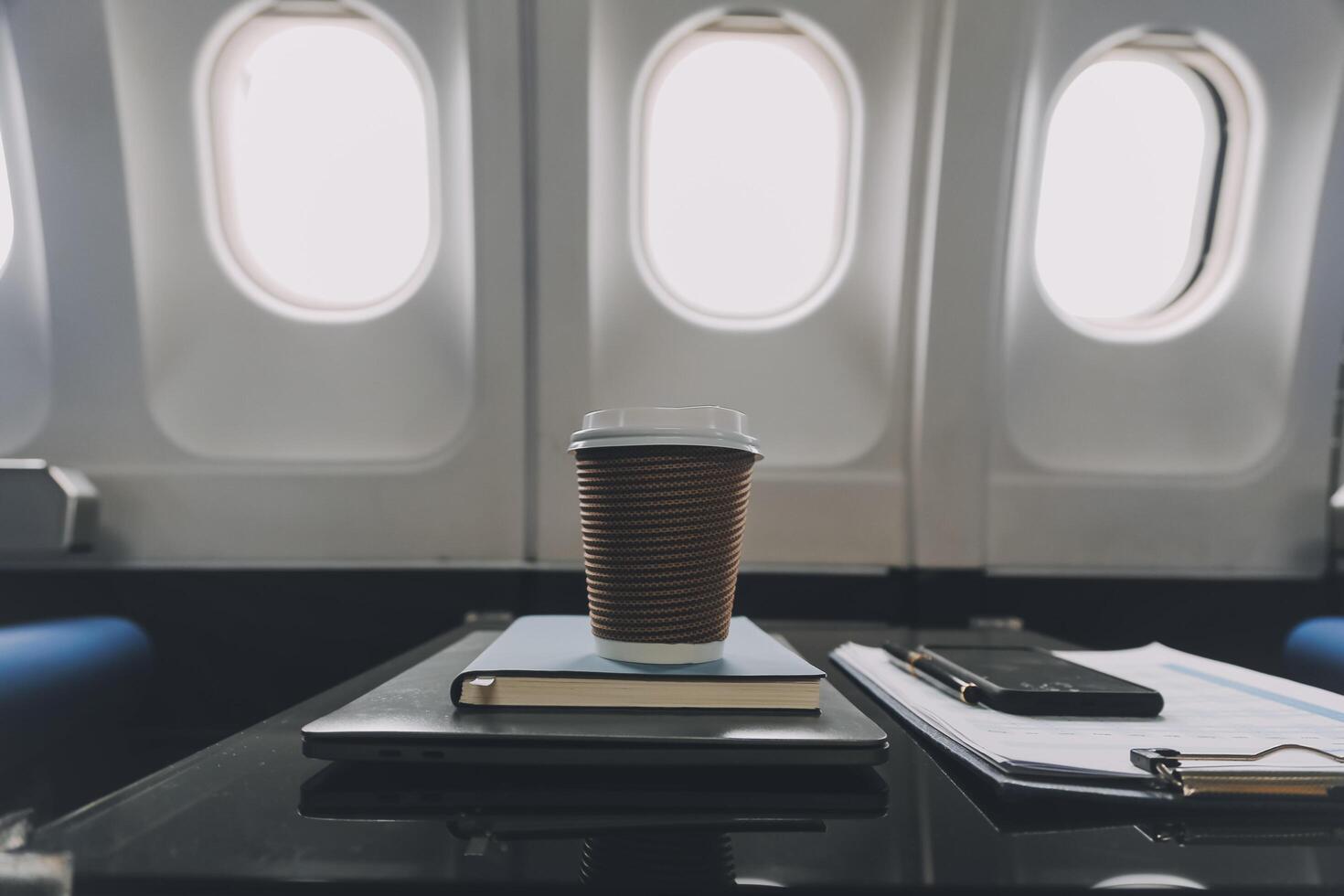 Cup of coffee with laptop and notebooks on table in airplane photo