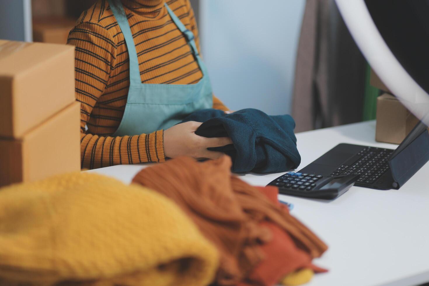 vlogger, blogger small SME business asian beautiful woman using mobile phone call for sell clothes live stream selling online, show product present detail at home office, entrepreneur ecommerce photo