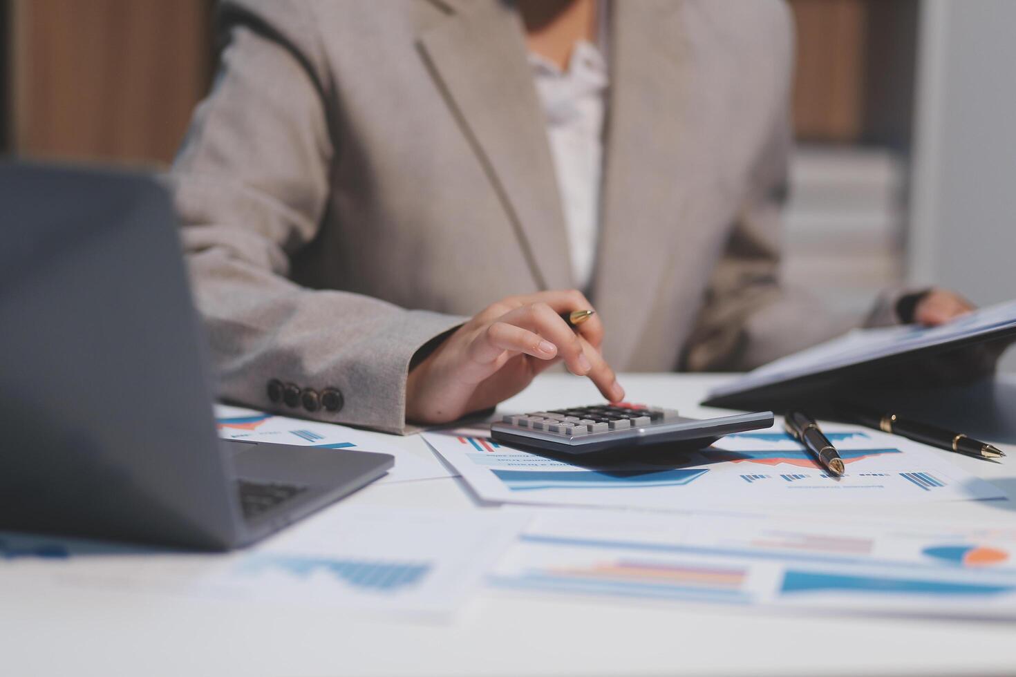 Business woman using calculator and writing make note with calculate. Woman working at office with laptop and documents on his desk photo