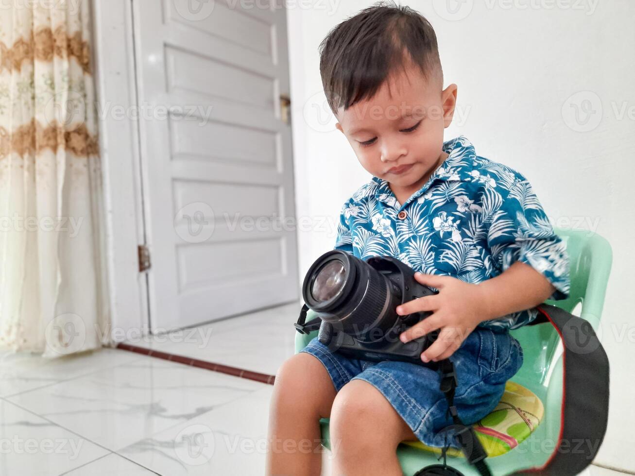 a boy sitting in a chair fiddling with a photography camera photo