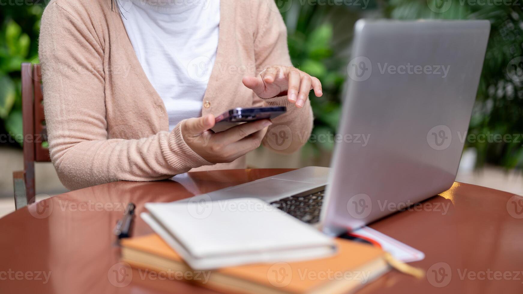 A cropped image of a woman using her smartphone while working remotely at a table outdoors. photo