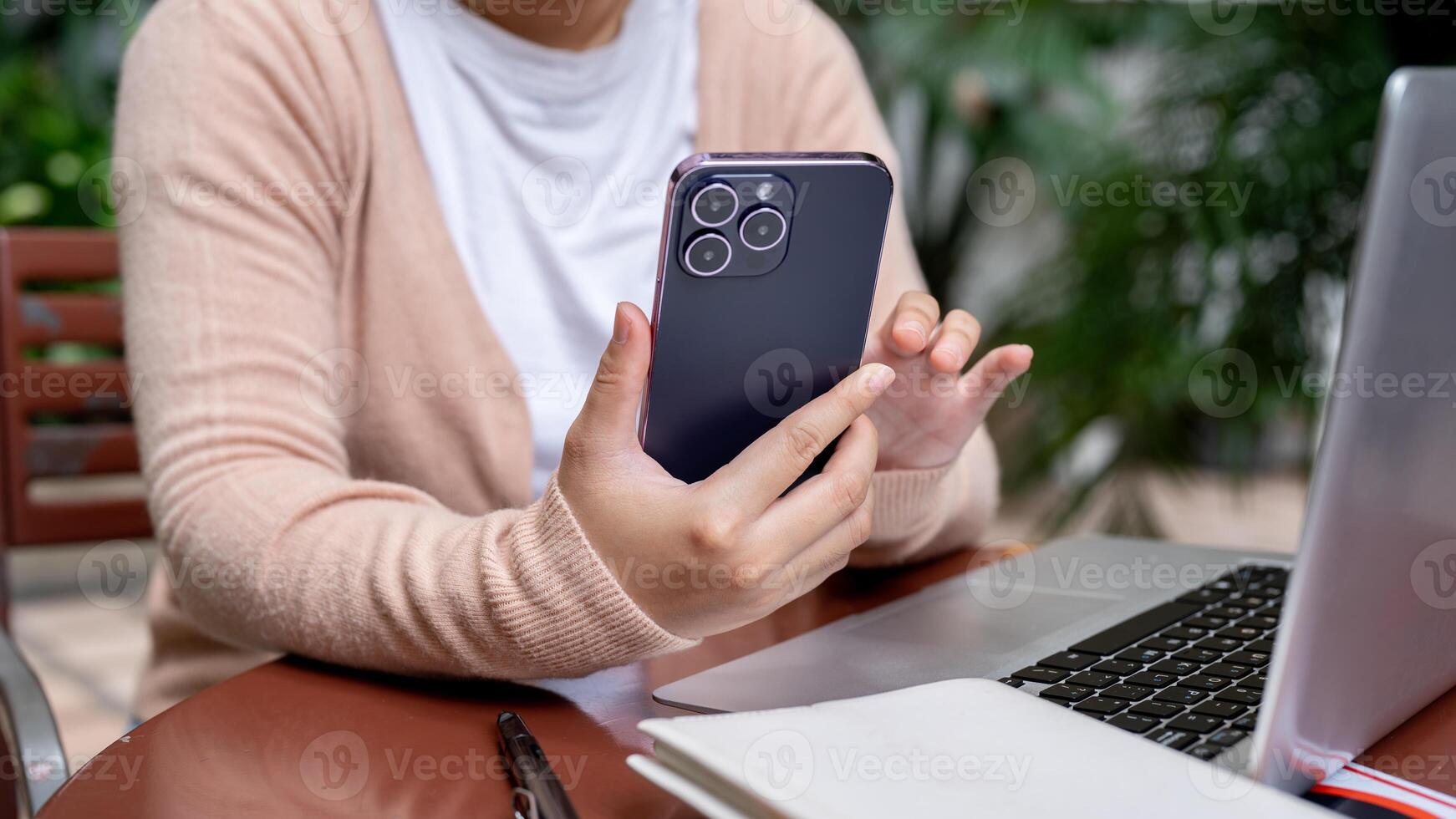 A cropped image of a woman using her smartphone at a table outdoors, checking messages. photo