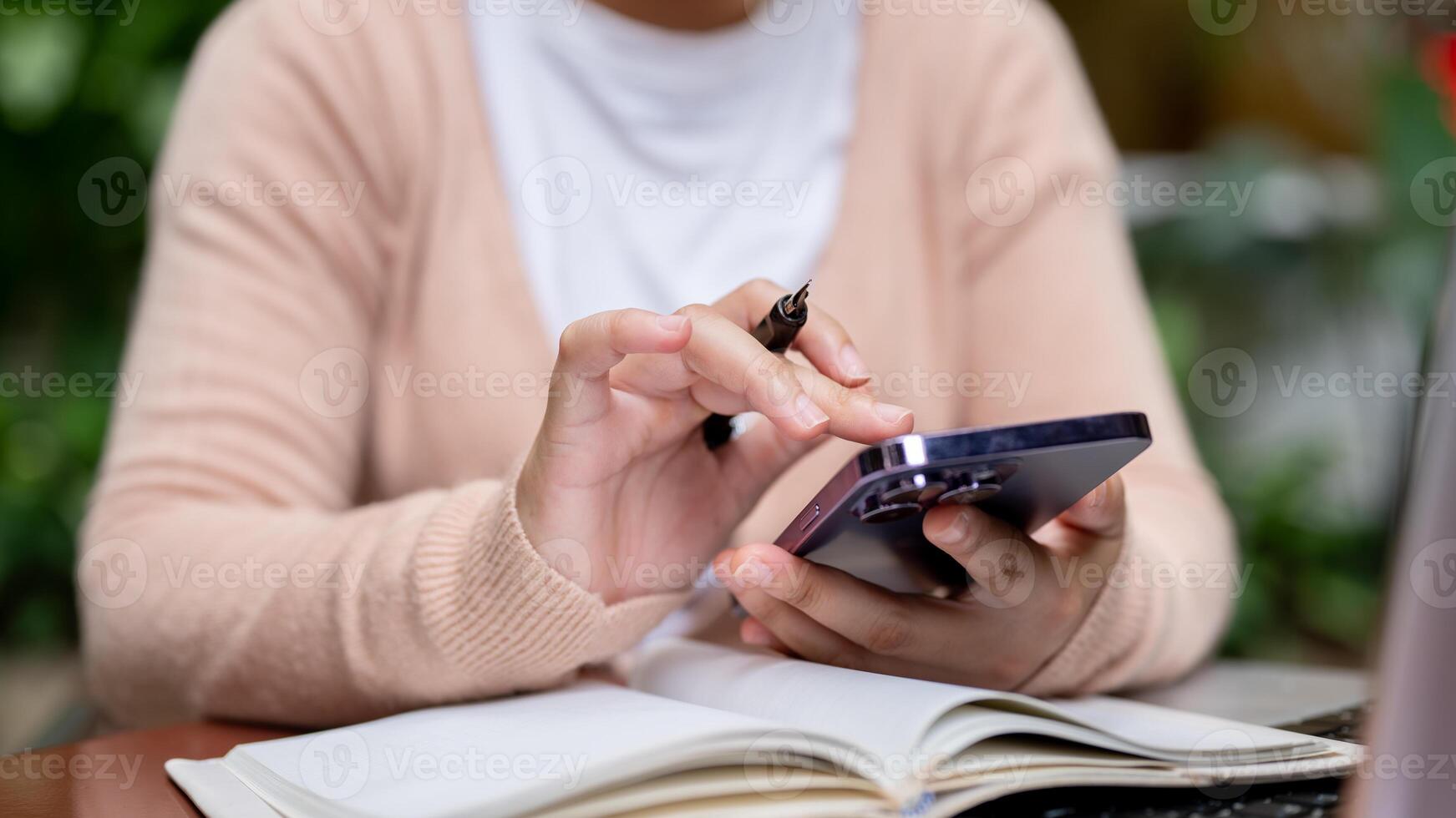 A close-up image of a woman using her smartphone while holding a pen, browsing the internet. photo