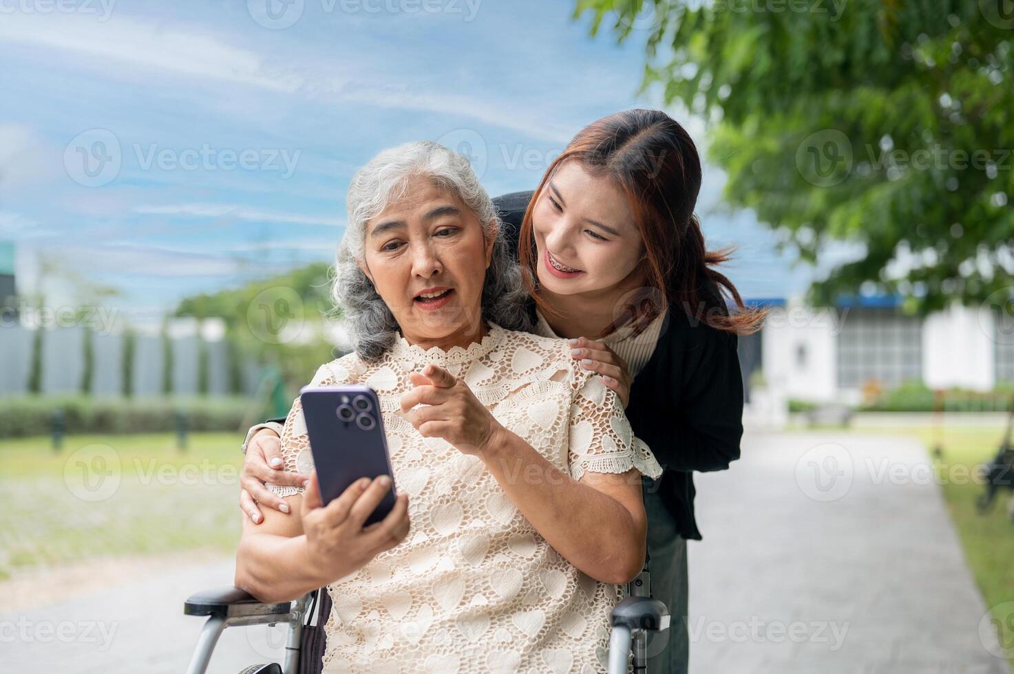 A lovely Asian granddaughter is hugging her grandma who is using a smartphone in a wheelchair. photo