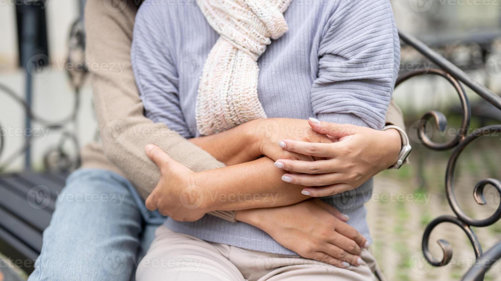 A cropped close-up image of a daughter hugging her mom while they sit on a bench outdoors together. photo