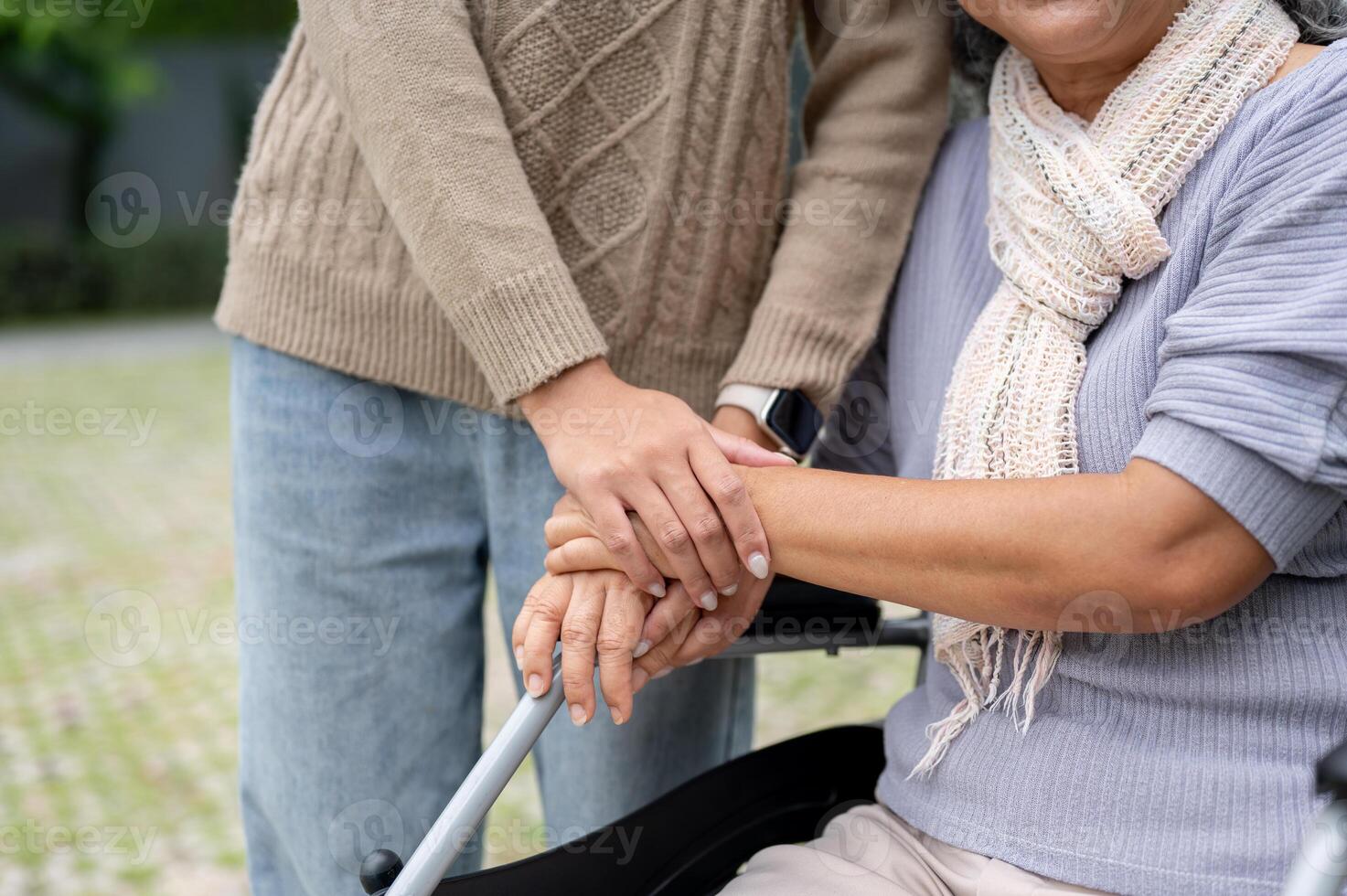 A close-up image of a daughter holding her mom's hand while she is in a wheelchair. photo
