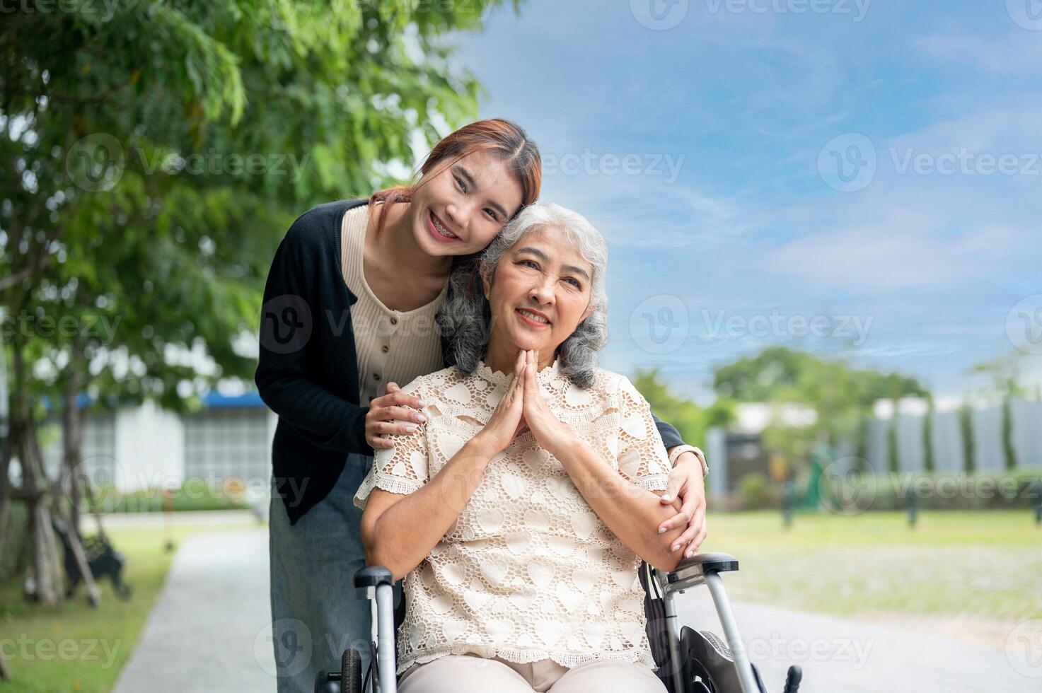 A lovely granddaughter is hugging her grandma, who is in a wheelchair, while walking her in a park. photo