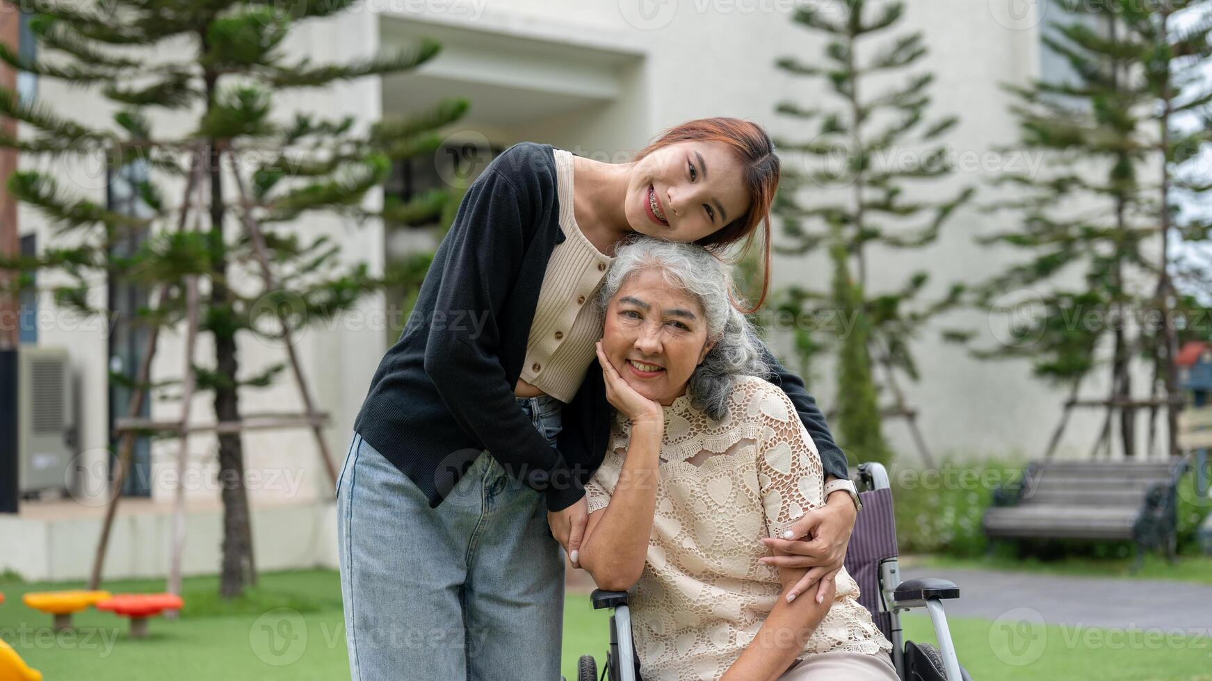 A lovely granddaughter is hugging her grandma, who is in a wheelchair, while walking her in a park. photo