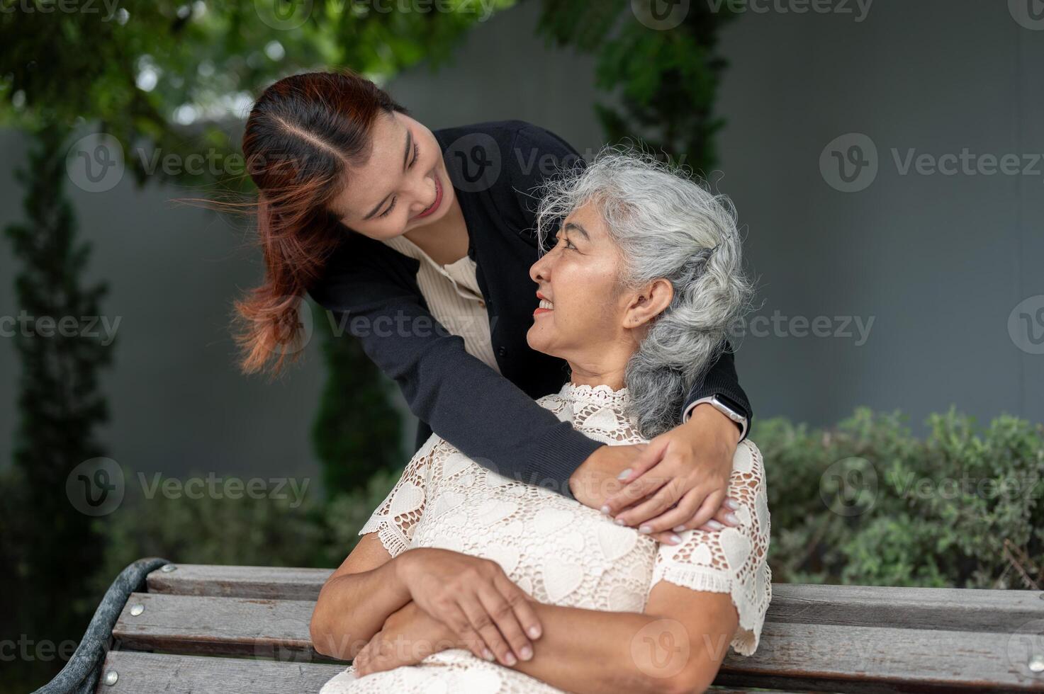 A lovely Asian granddaughter is embracing her grandma with love while resting in a garden together. photo