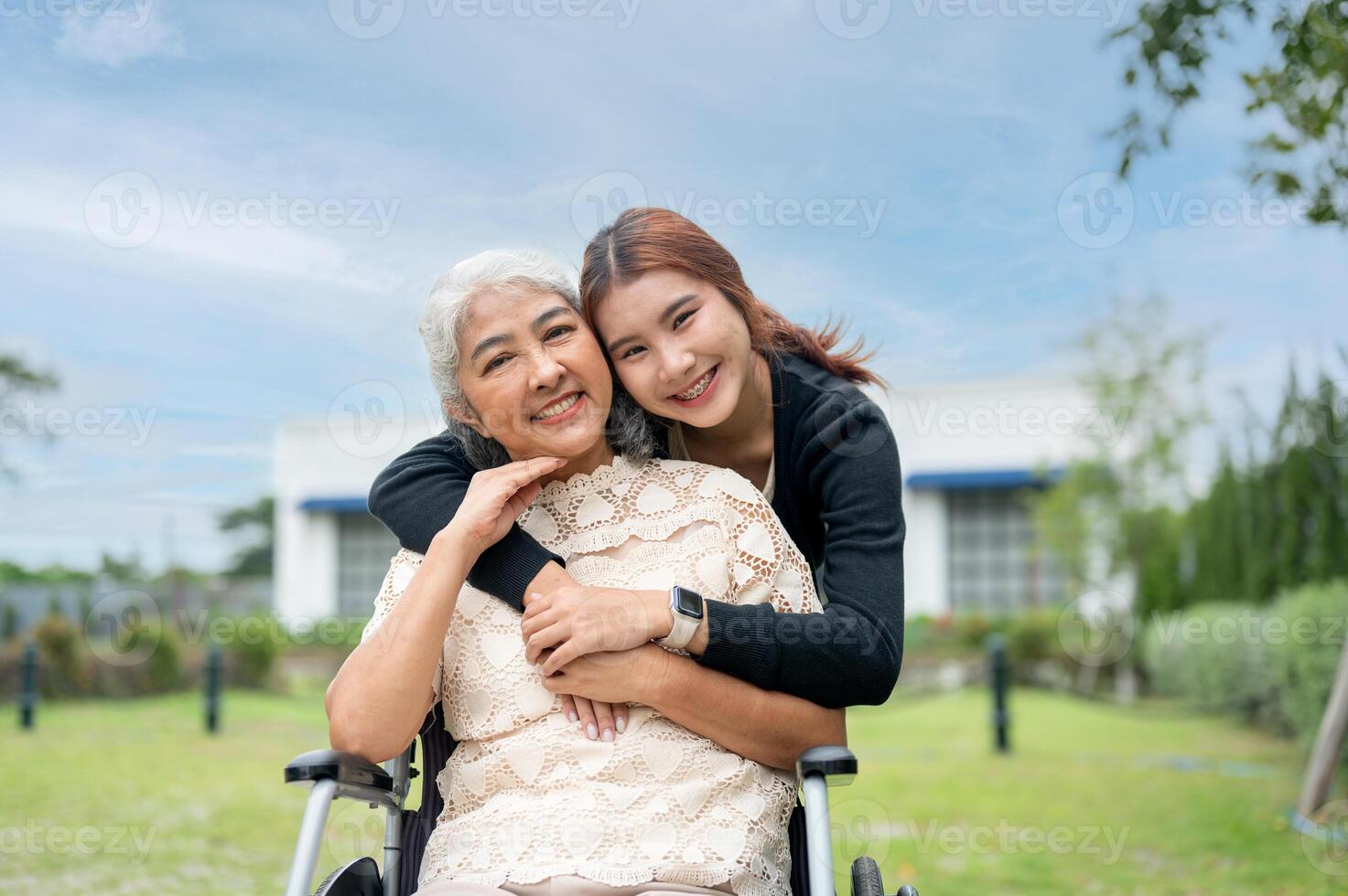 A lovely granddaughter is hugging her grandma, who is in a wheelchair, while walking her in a park. photo