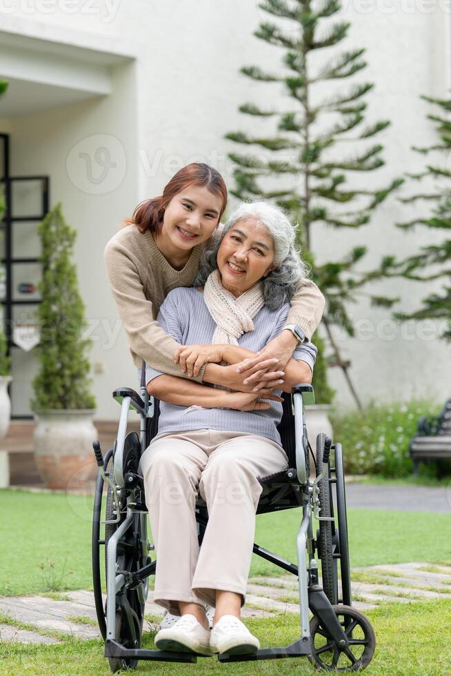 A lovely Asian granddaughter and a happy retired grandma in a wheelchair are in their home backyard. photo