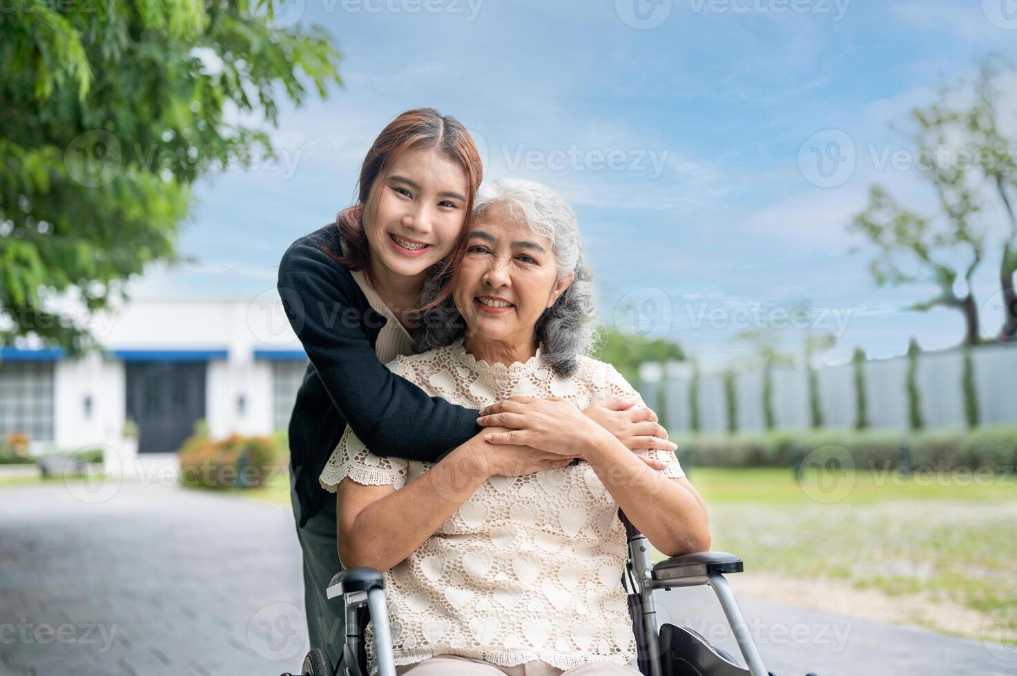 A happy, positive retired Asian grandma in a wheelchair is in a park with her lovely granddaughter. photo