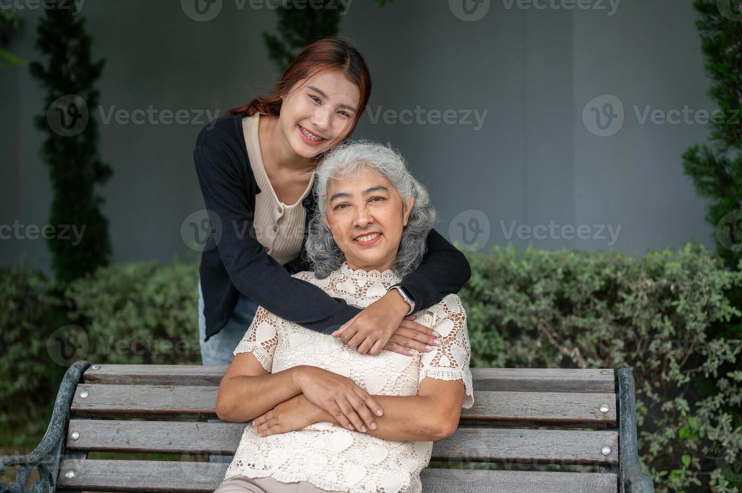A lovely Asian granddaughter is embracing her grandma with love while resting in a garden together. photo
