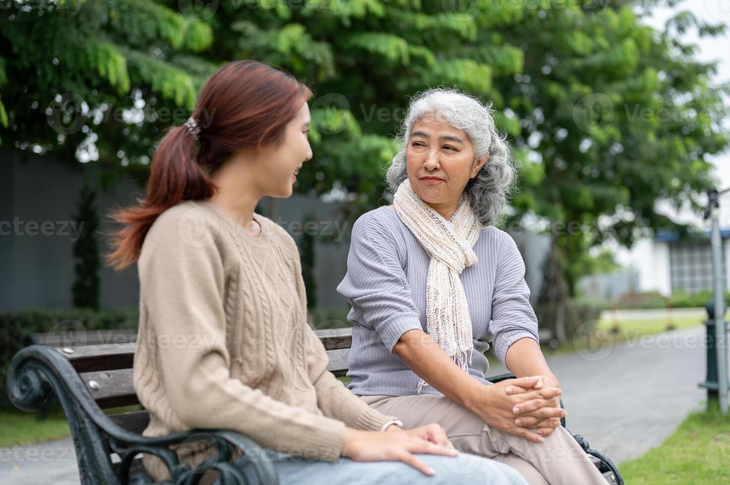 A lovely Asian granddaughter and a caring grandma are having a conversation in a park together. photo