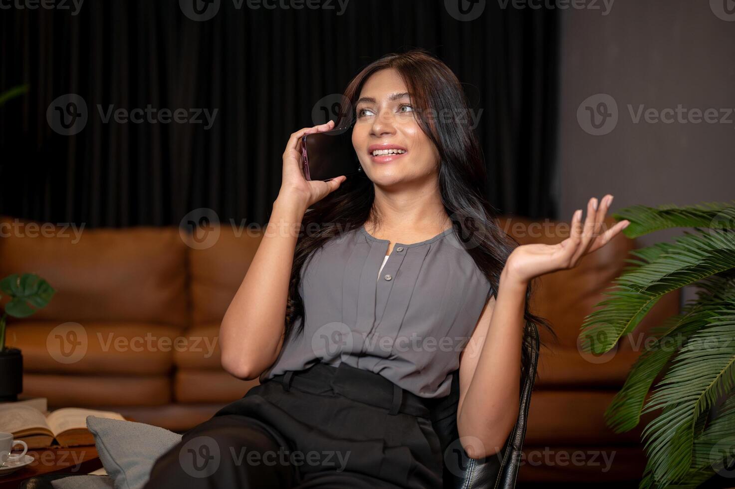 A beautiful Asian businesswoman is talking on the phone with a client while sitting on a chair. photo