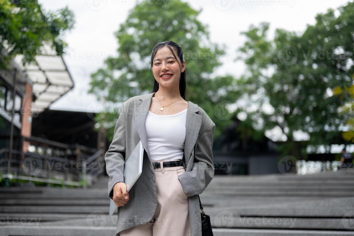An attractive Asian businesswoman in a business suit is smiling at the camera, standing in the city. photo