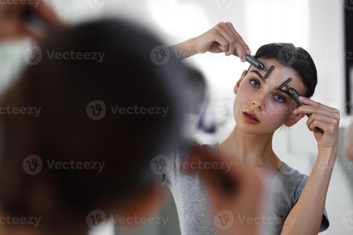 A young woman massages her face with gouache while looking in the mirror. photo