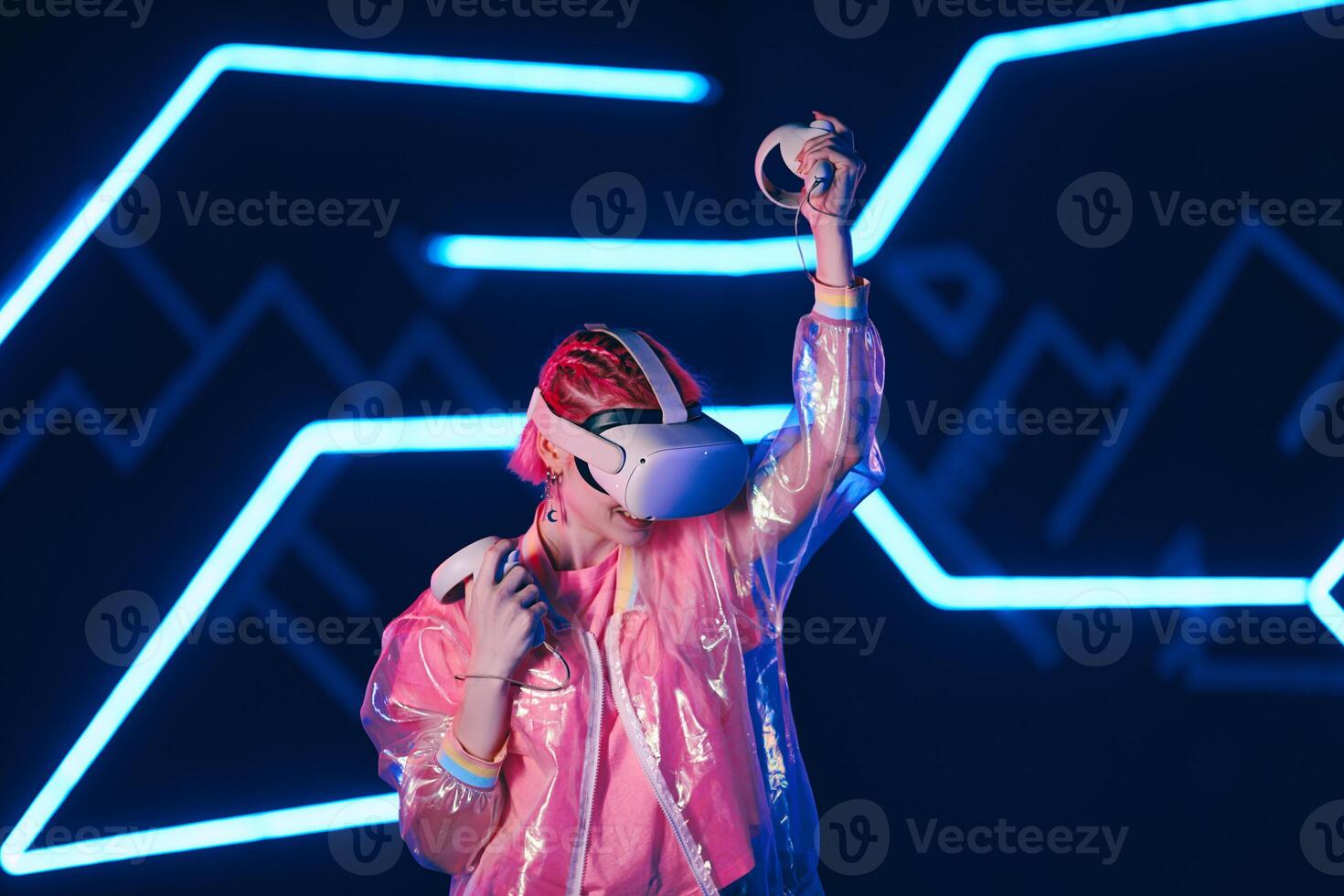 Young female gamer in pink is playing virtual reality games. VR headset and controllers. photo