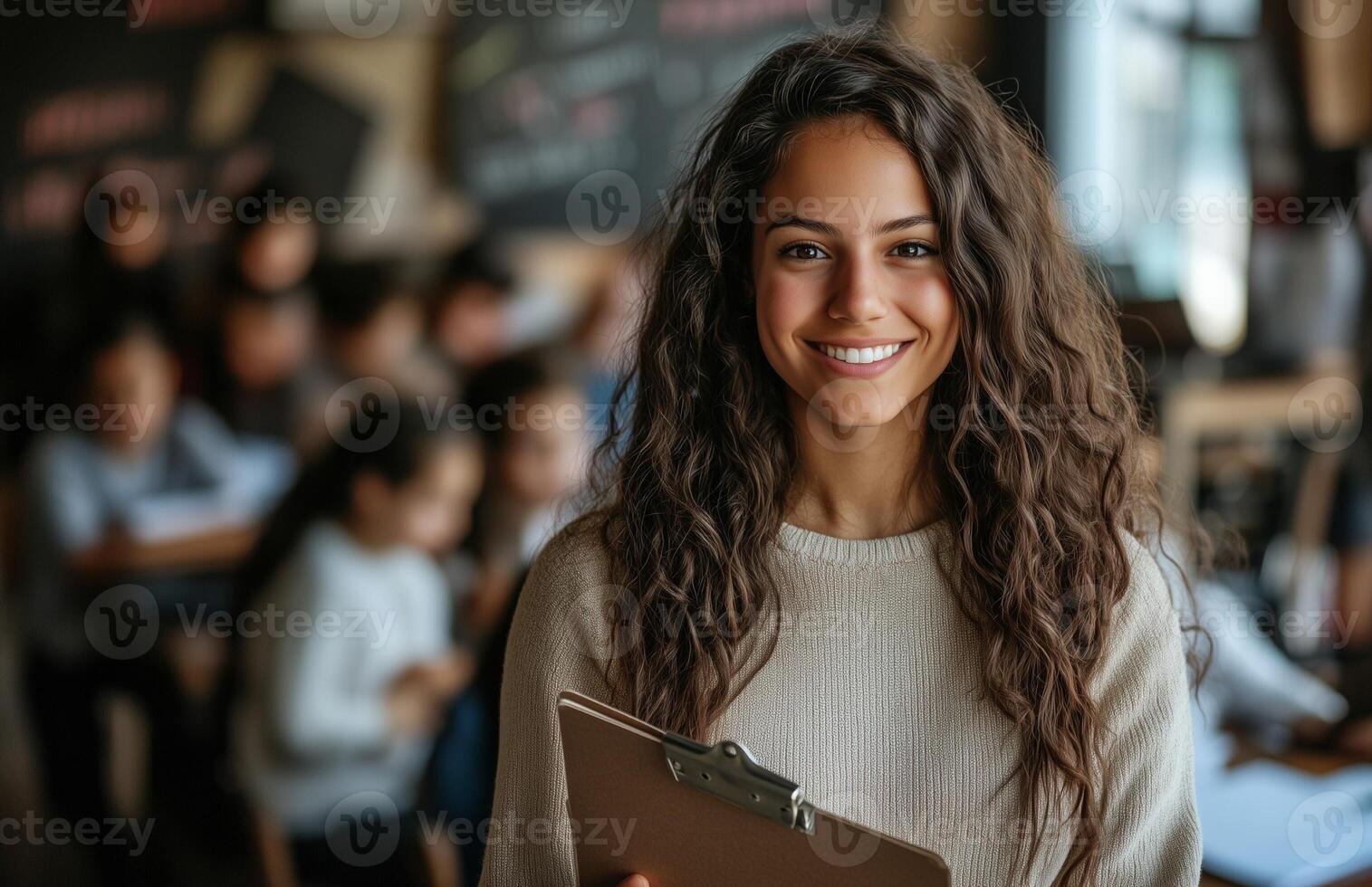 Female teacher smiling at camera holding clipboard with students doing homework in classroom setting photo