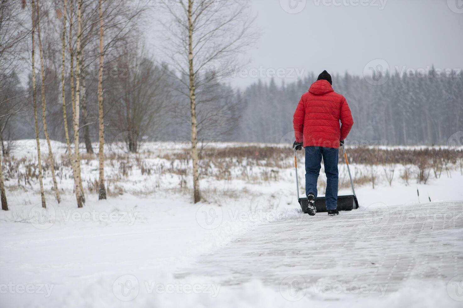 Man with a snow shovel cleans the pavement in the yard. Man shoveling snow after a winter storm photo