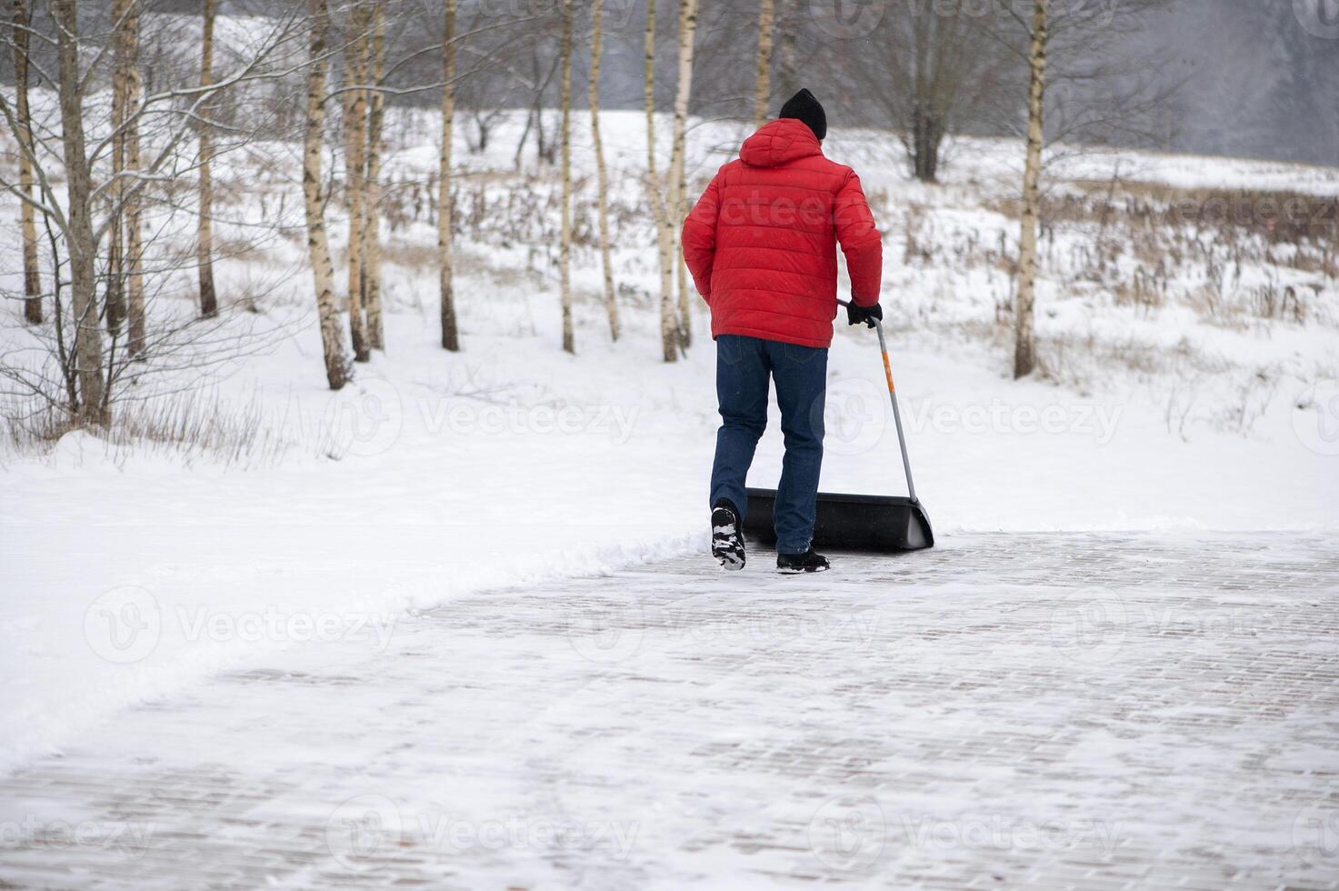Man with a snow shovel cleans the pavement in the yard. Man shoveling snow after a winter storm photo