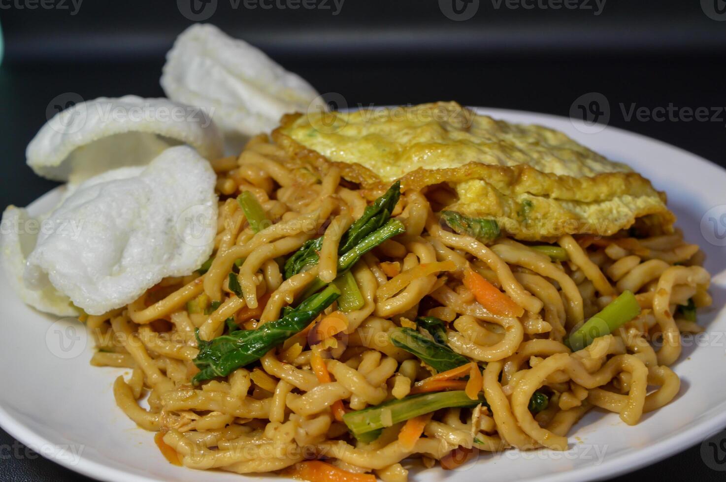 Mie goreng or fried noodles are one of the most popular foods in Southeast Asia, including Indonesia. Served with eggs and vegetables, on a plate photo