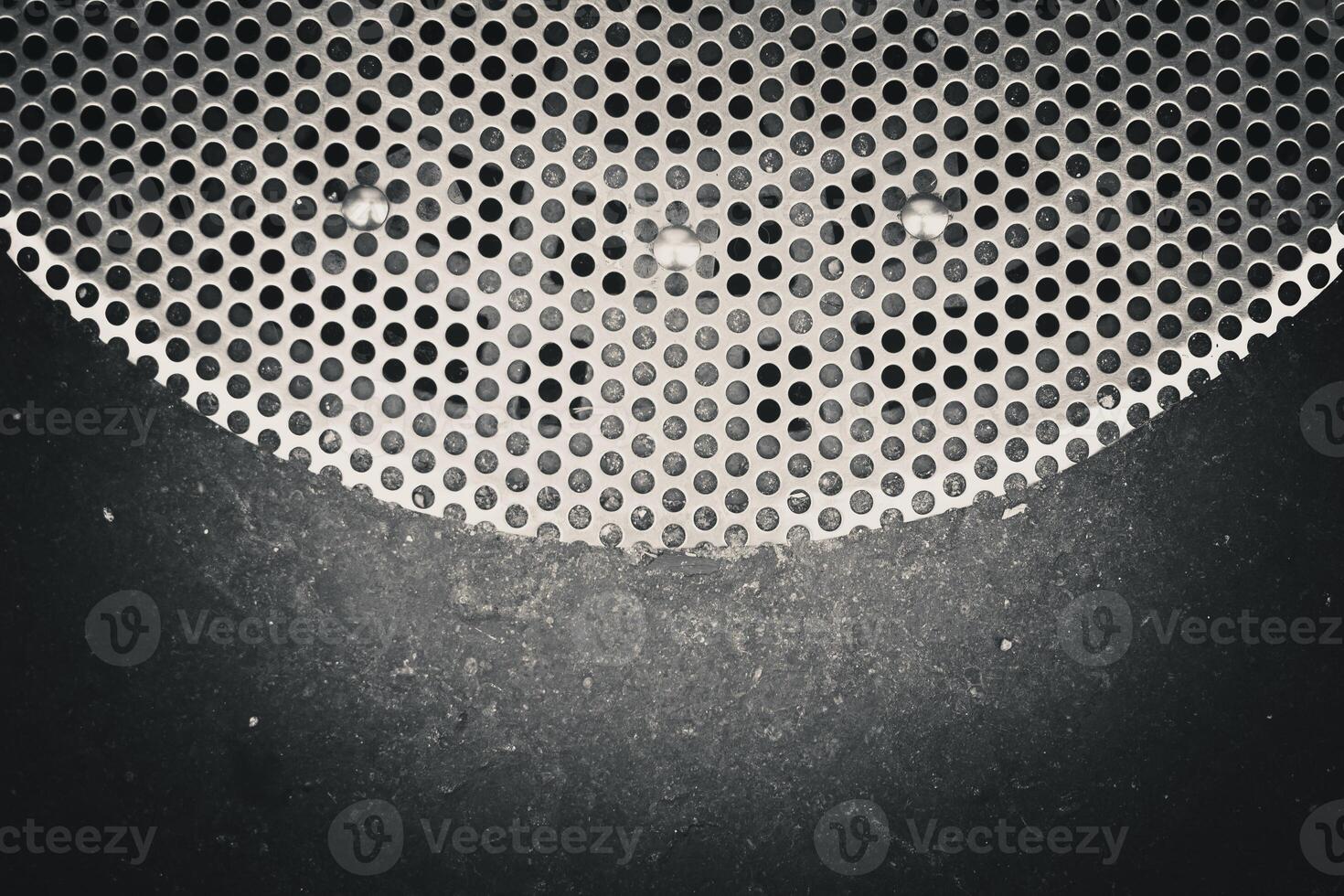 closeup of a surface with a pattern of circular holes in a metal grille or perforated sheet photo