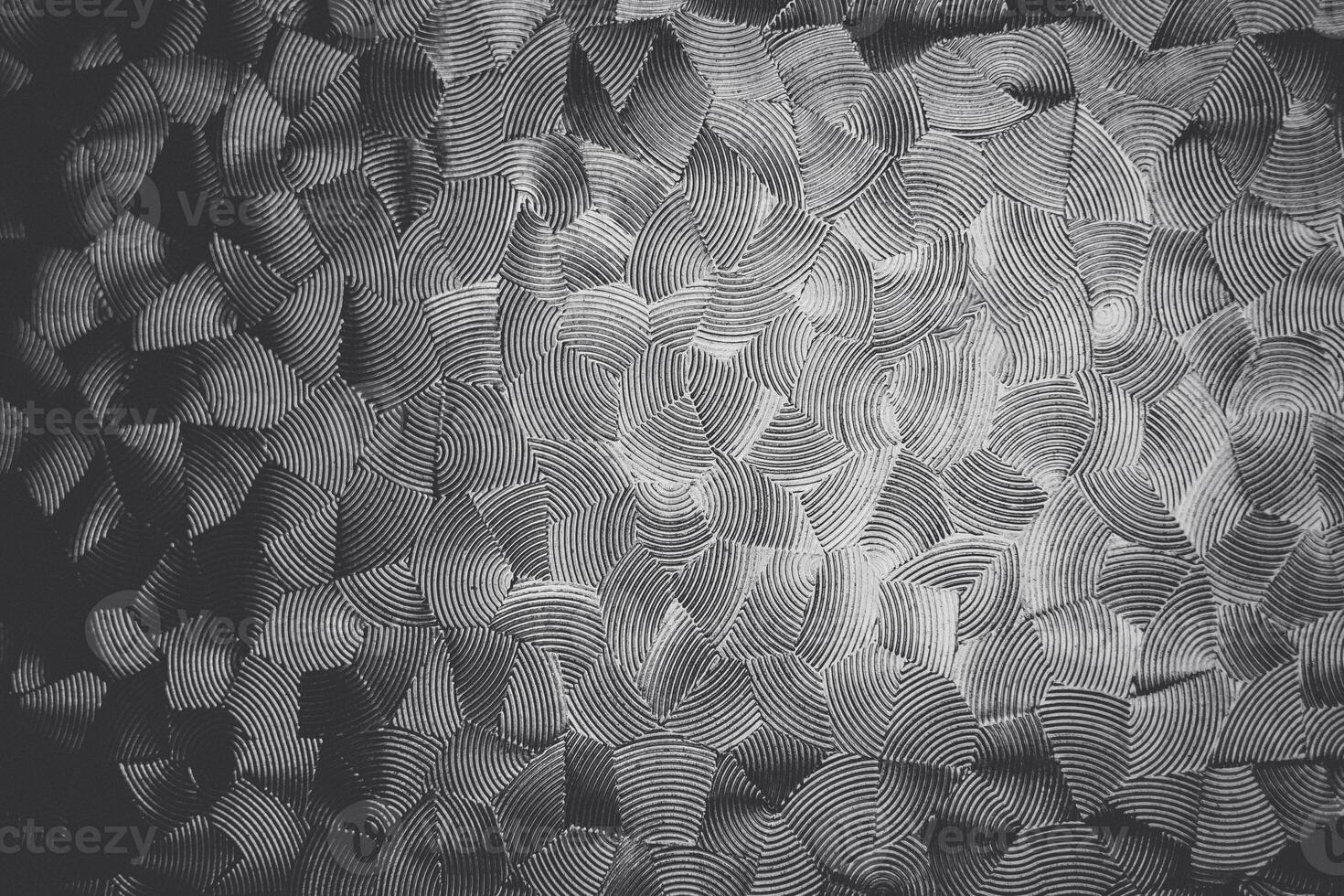 Monochromatic, textured pattern on glass with overlapping, undulating lines that create an illusion of three-dimensional waves on a flat surface photo