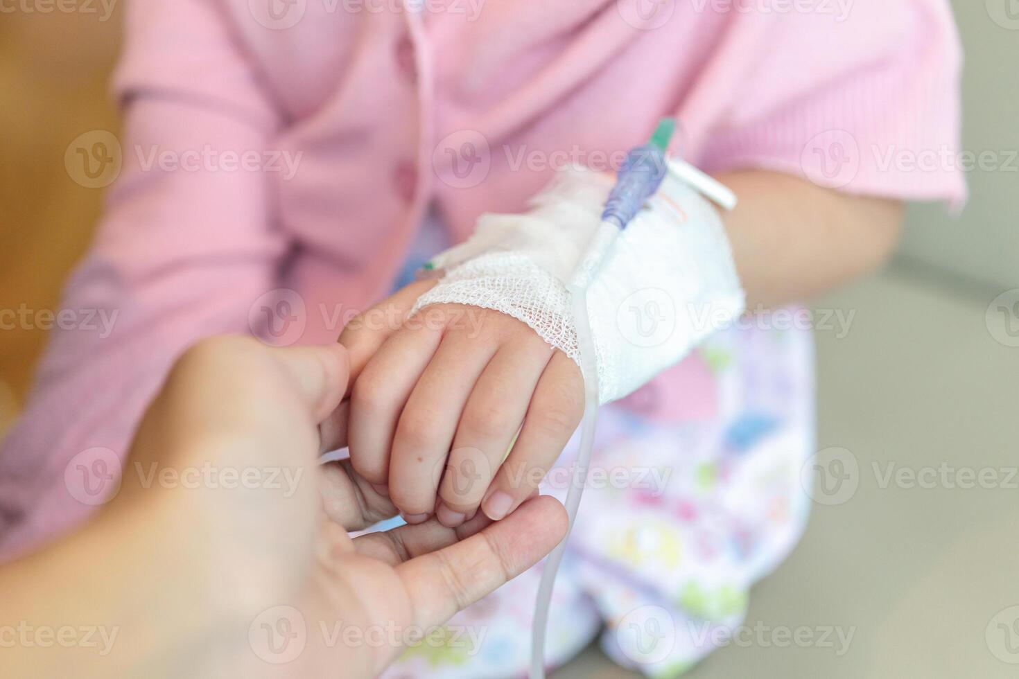 Mother holding child hand with saline IV solution in hospital photo
