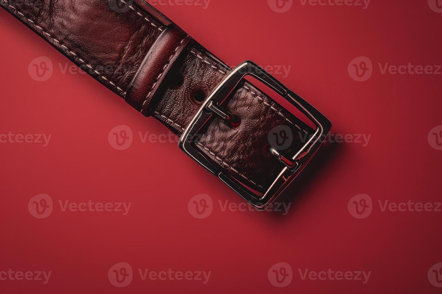 Brown leather belt with metal buckle lying on red background photo