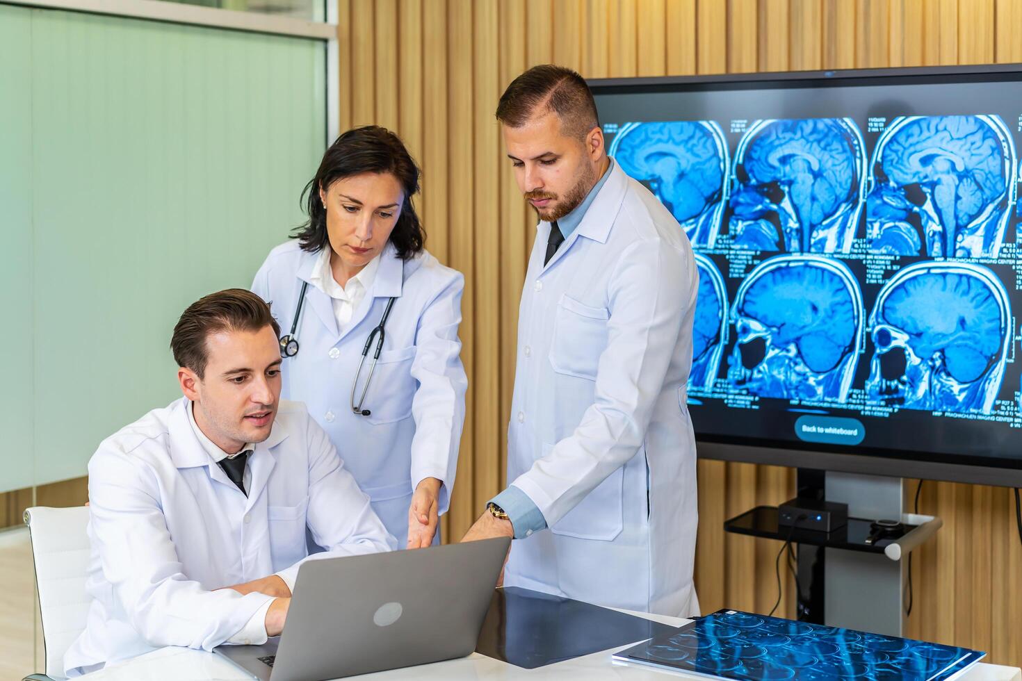 equipo de Tres doctores discute el resultados de un mri escanear de el del paciente cabeza en el consultante habitación de moderno hospital, médico que se discute acerca de tratamiento para paciente mirando en ordenador portátil foto