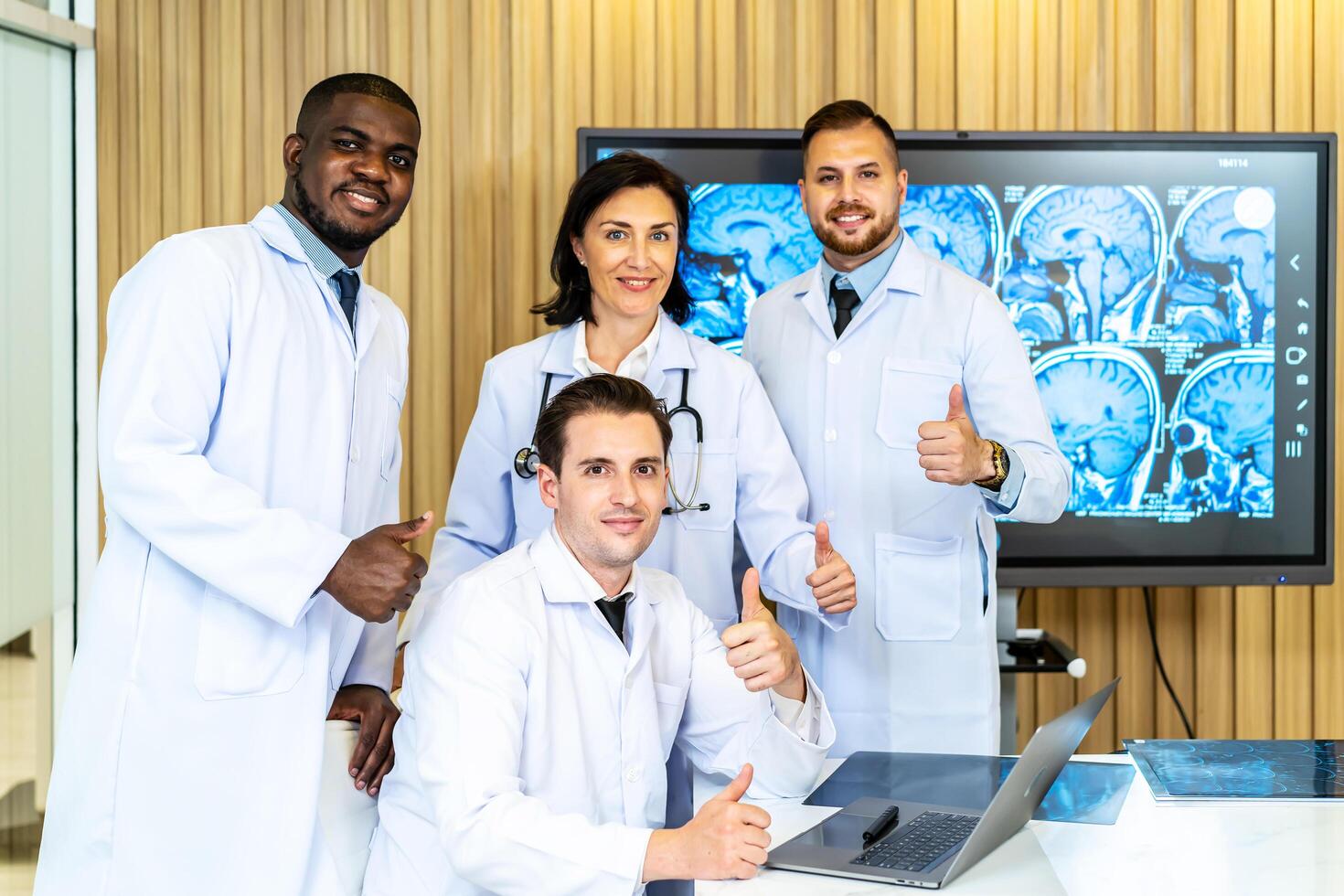 Group of medical practitioners in lab coats gesturing thumbs up while sitting and standing with smiling on camera. Four colleagues discusses the results of an MRI scan of the patient's head photo