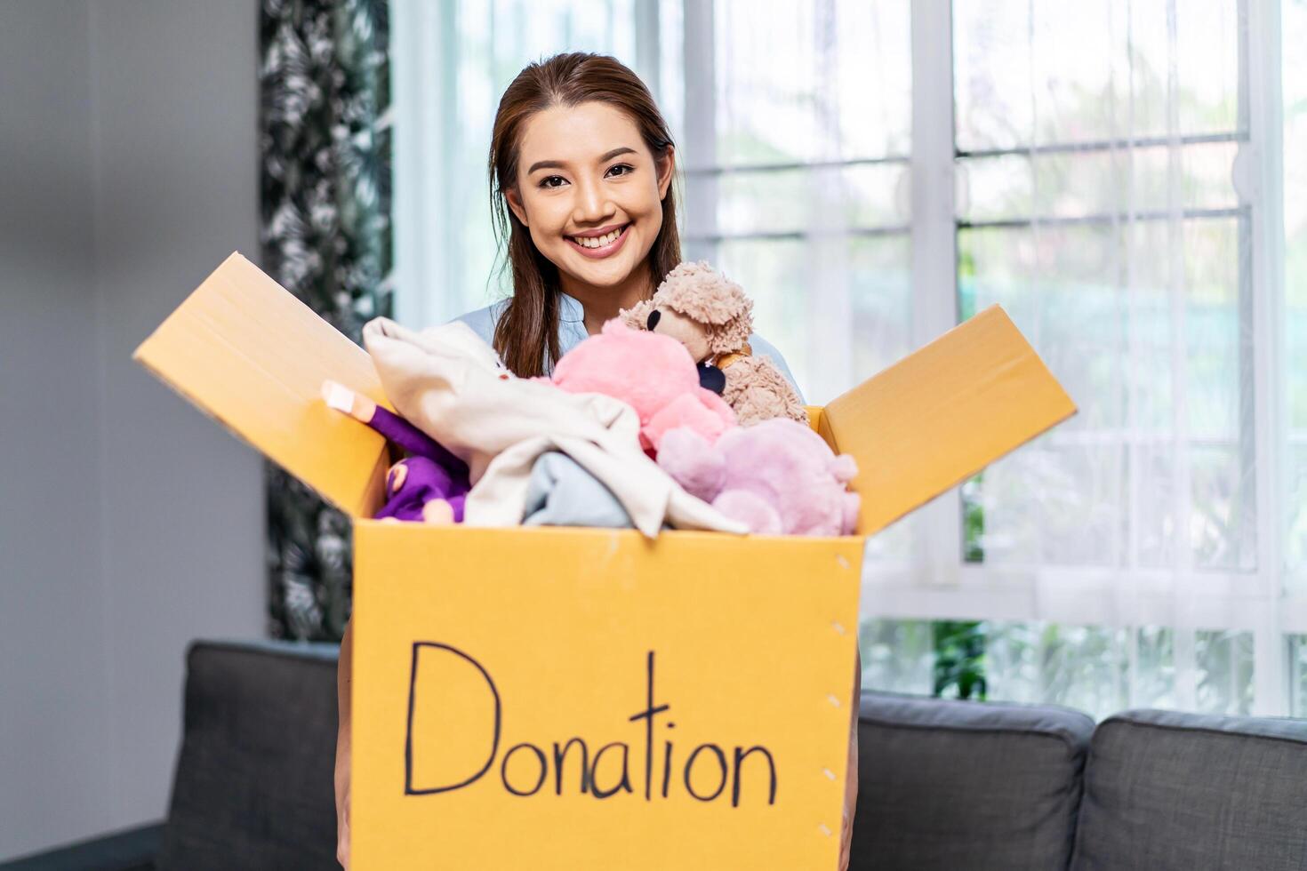 Donation Concept. Happy volunteer asian woman holding a Donate Box with full of toy doll, She working at charity center. photo