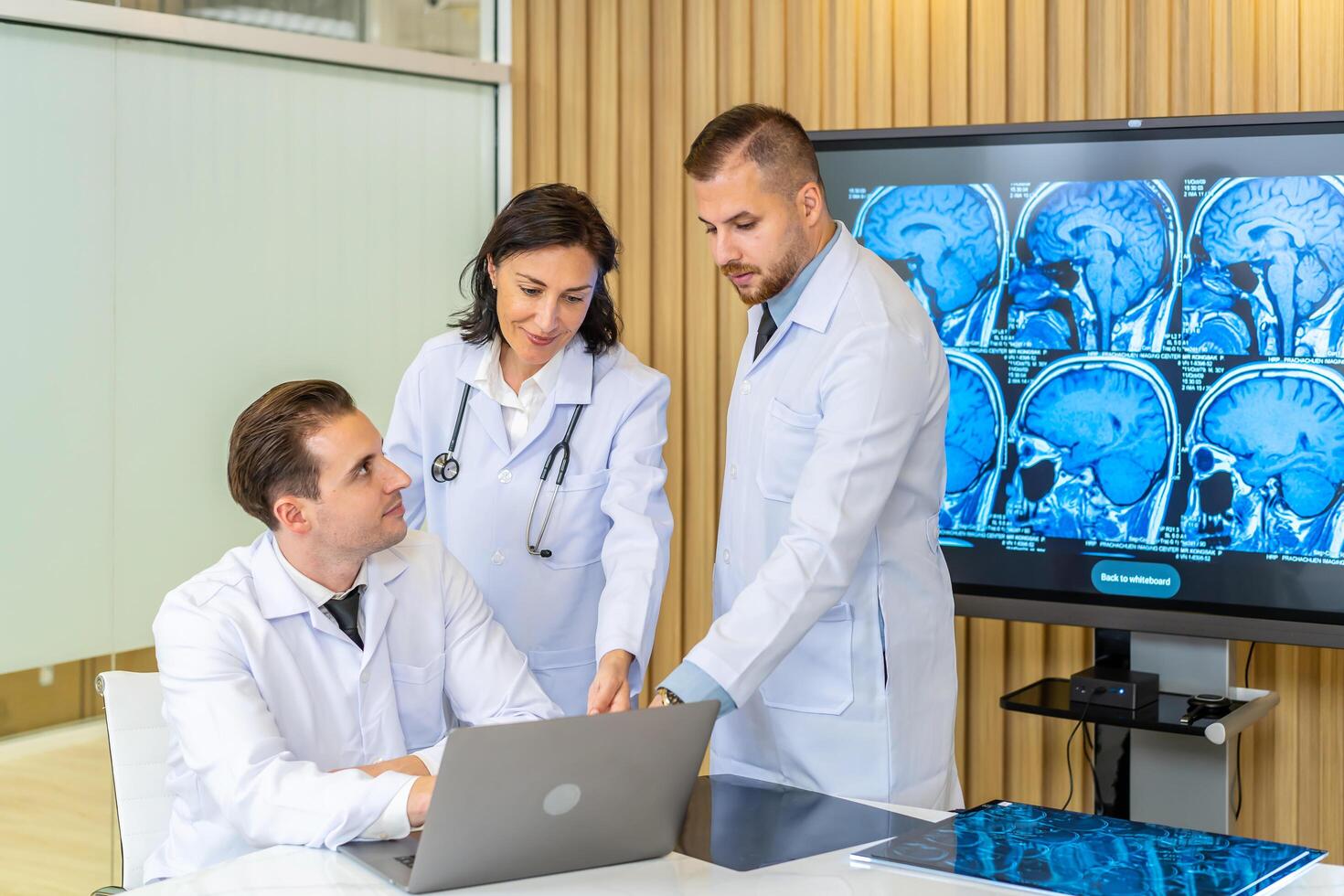 Team of three doctors discusses the results of an MRI scan of the patient's head in the consulting room of modern hospital, physician discussing about treatment for patient looking in laptop photo