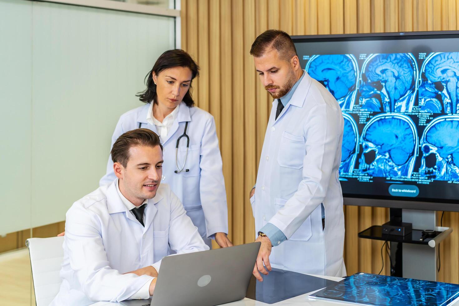 equipo de Tres doctores discute el resultados de un mri escanear de el del paciente cabeza en el consultante habitación de moderno hospital, médico que se discute acerca de tratamiento para paciente mirando en ordenador portátil foto