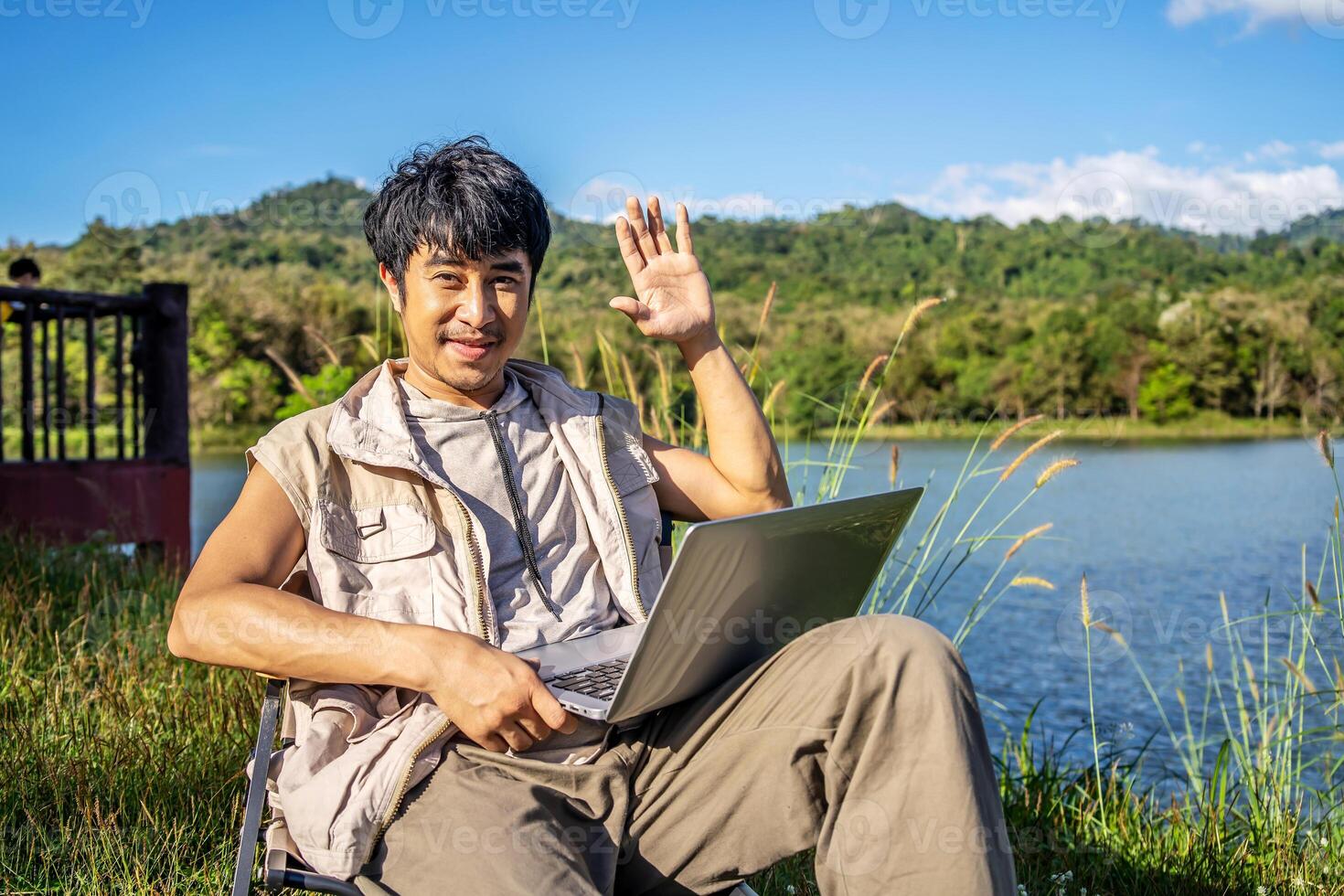 Young travel man relax and enjoy talking calling on on laptop, using laptop computer work remotely anywhere using internet connected to portable solar panel charging photo