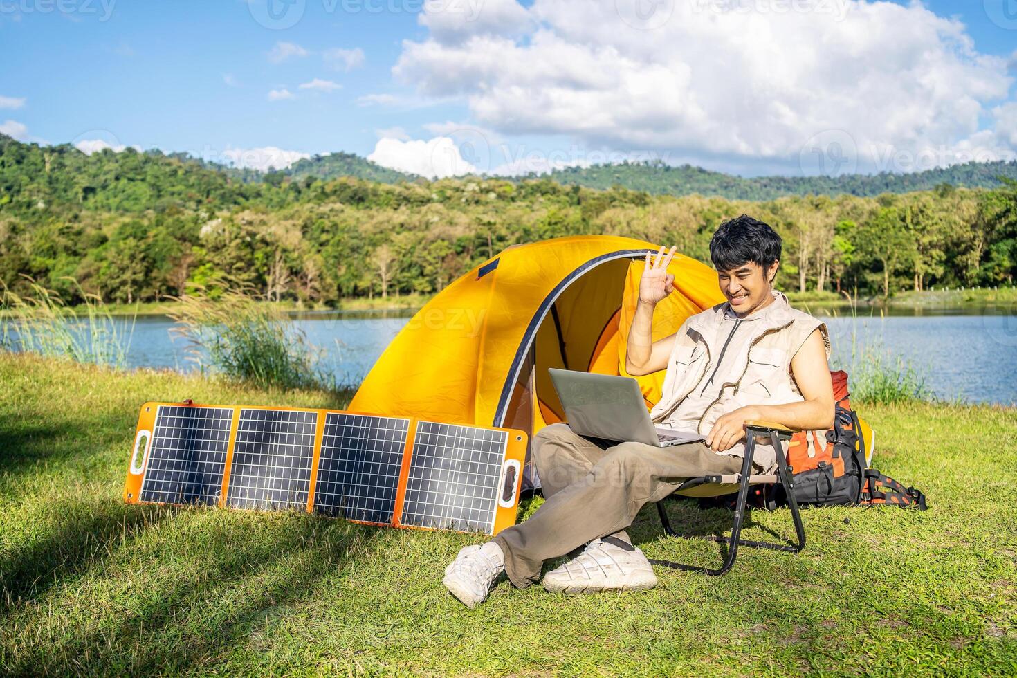 Young travel man relax and enjoy talking calling on on laptop, using laptop computer work remotely anywhere using internet connected to portable solar panel charging photo