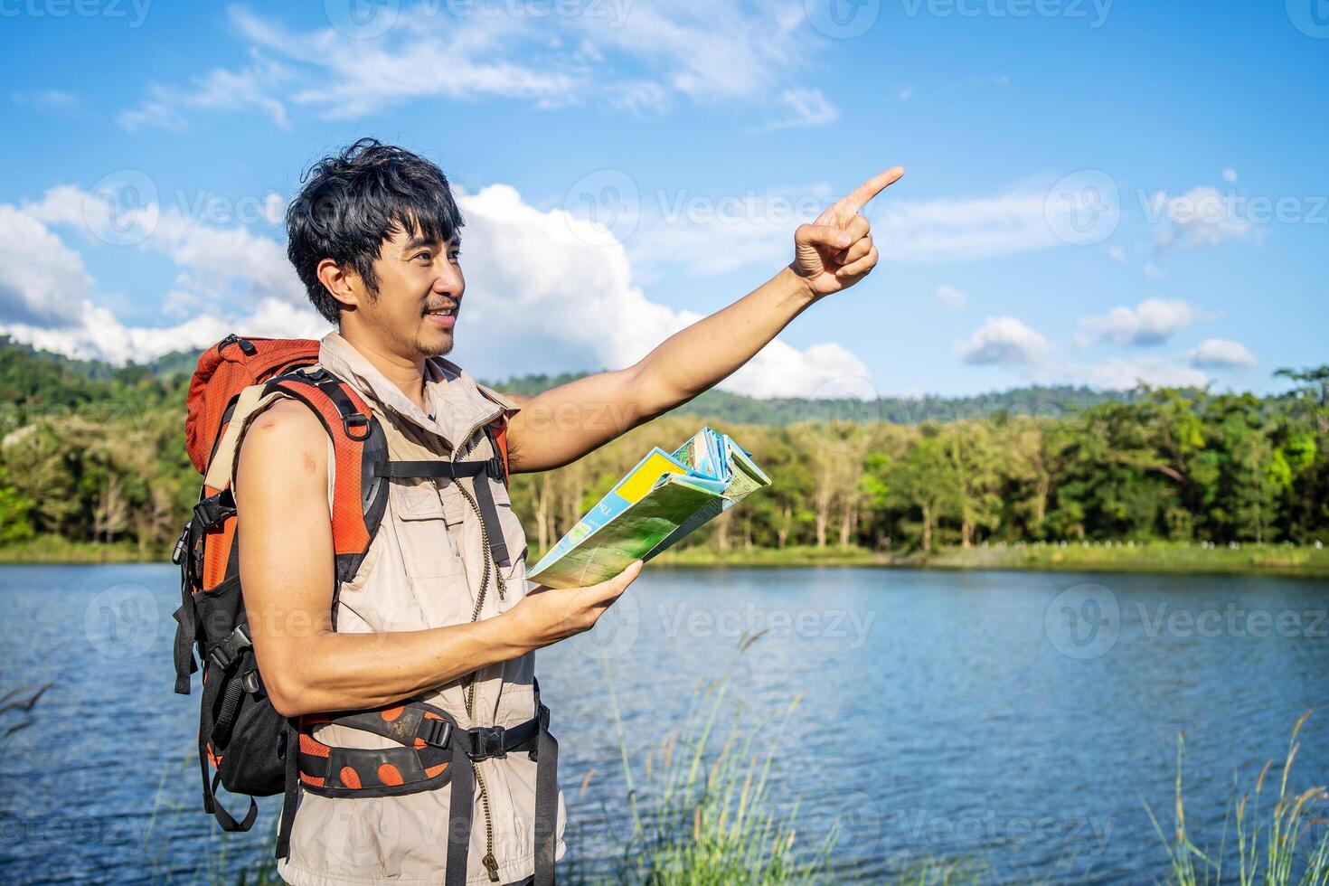 Young asian attractive male tourists looking for map in forest, Lost hiker male with backpacks reading travel map, Navigating and looking for directions in pine forest. Trekking concept. photo